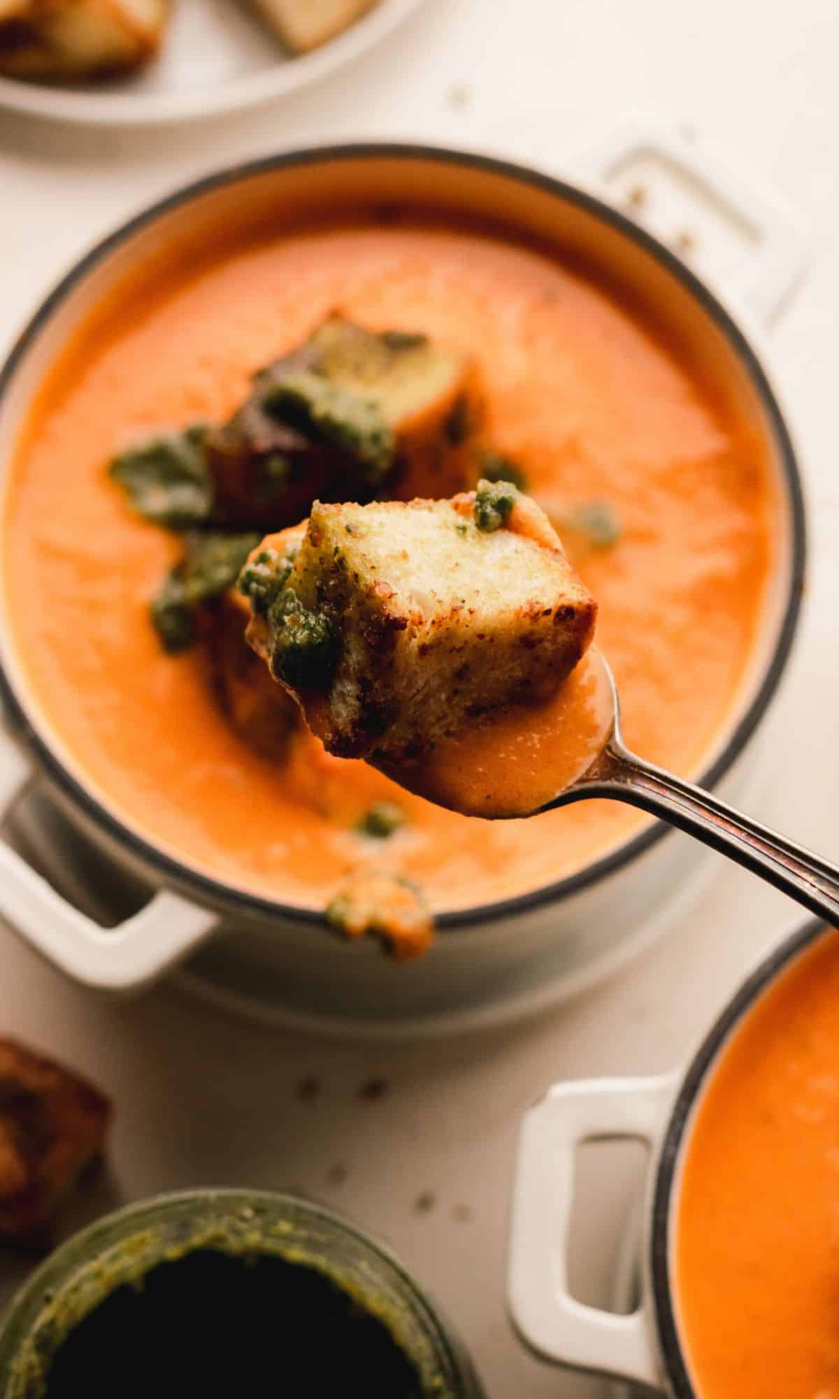 A spoonful of roasted tomato soup in mini Dutch ovens topped with pesto croutons.