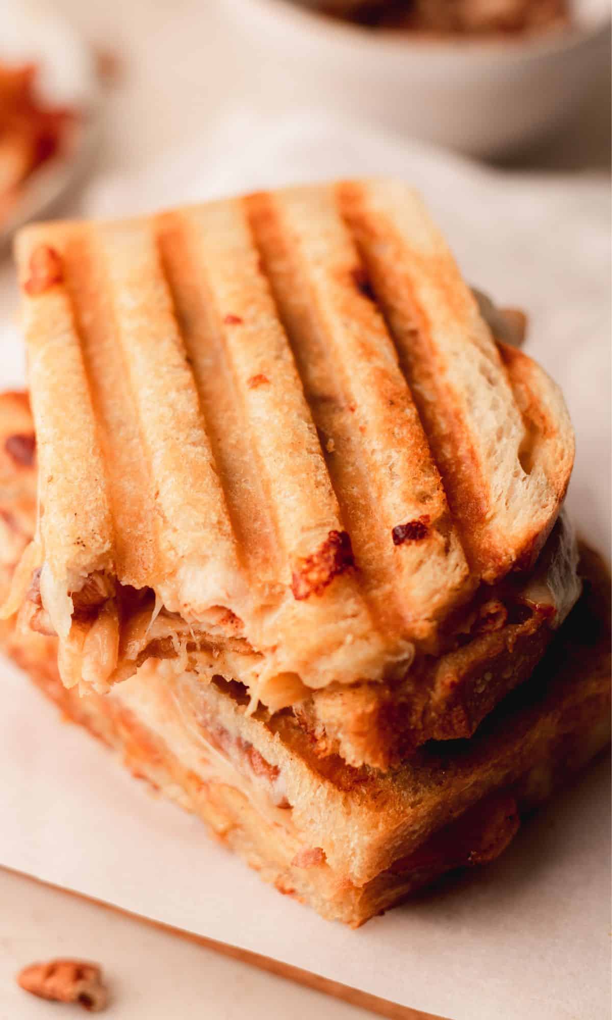 A stack of roasted apple and chicken panini halves with a bite taken out of the one on top.