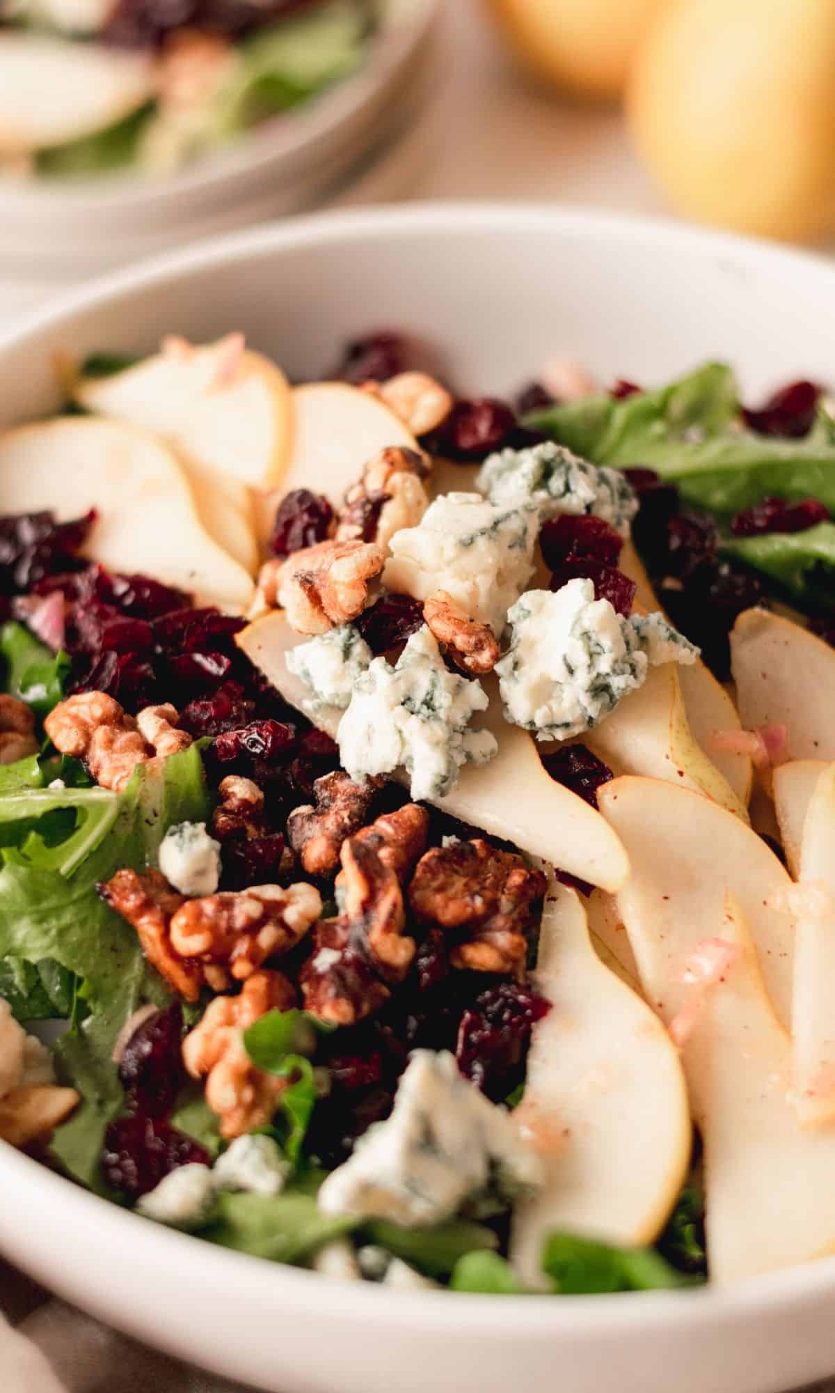 Pear, blue cheese, and toasted walnut salad in a white bowl.