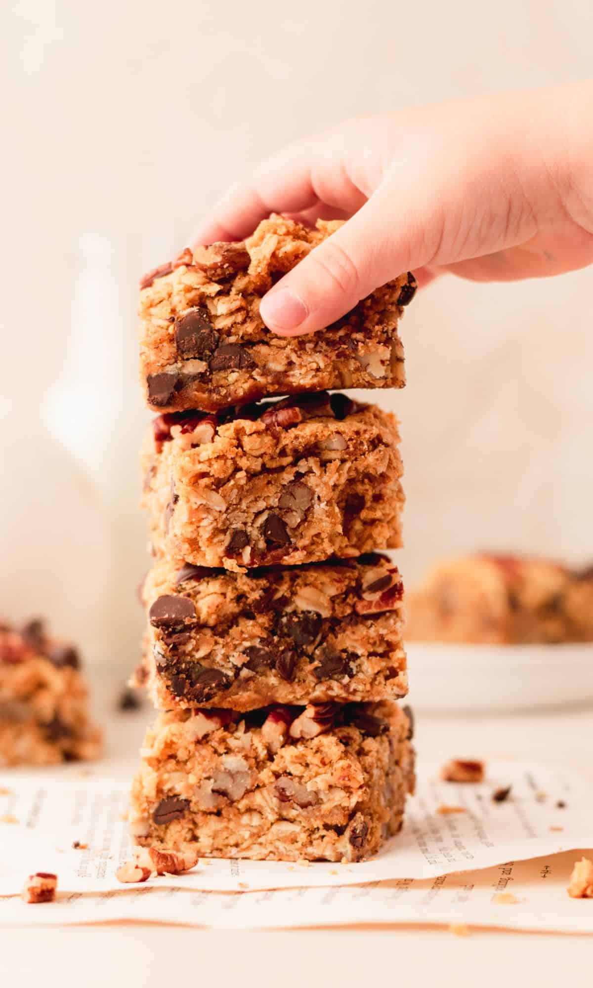 A stack of four pumpkin oatmeal bars and a hand taking the top one off.