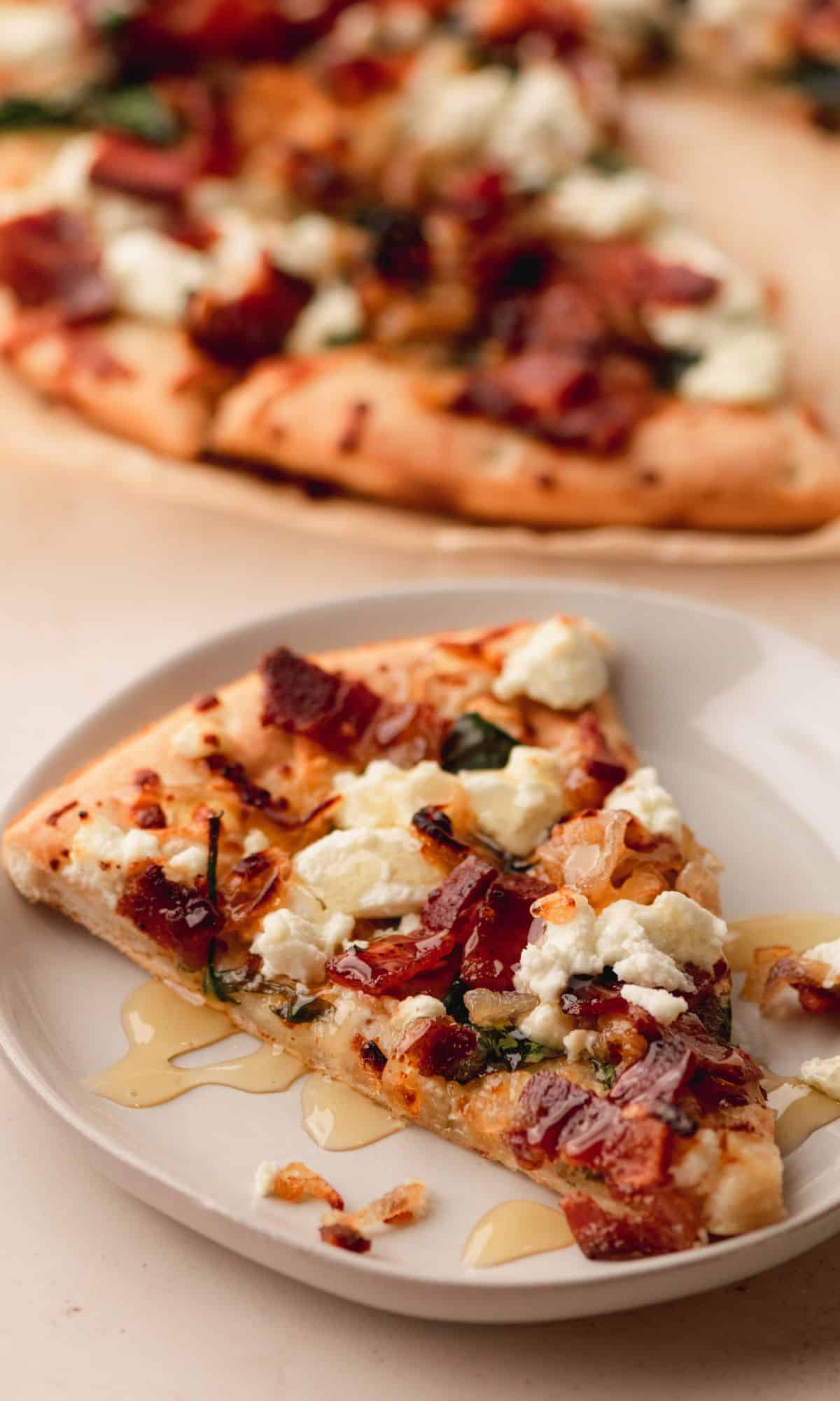 Caramelized shallot and bacon goat cheese pizza on a white plate drizzled with honey.