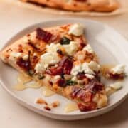 Bacon goat cheese pizza with caramelized shallots on a white plate drizzled with honey.