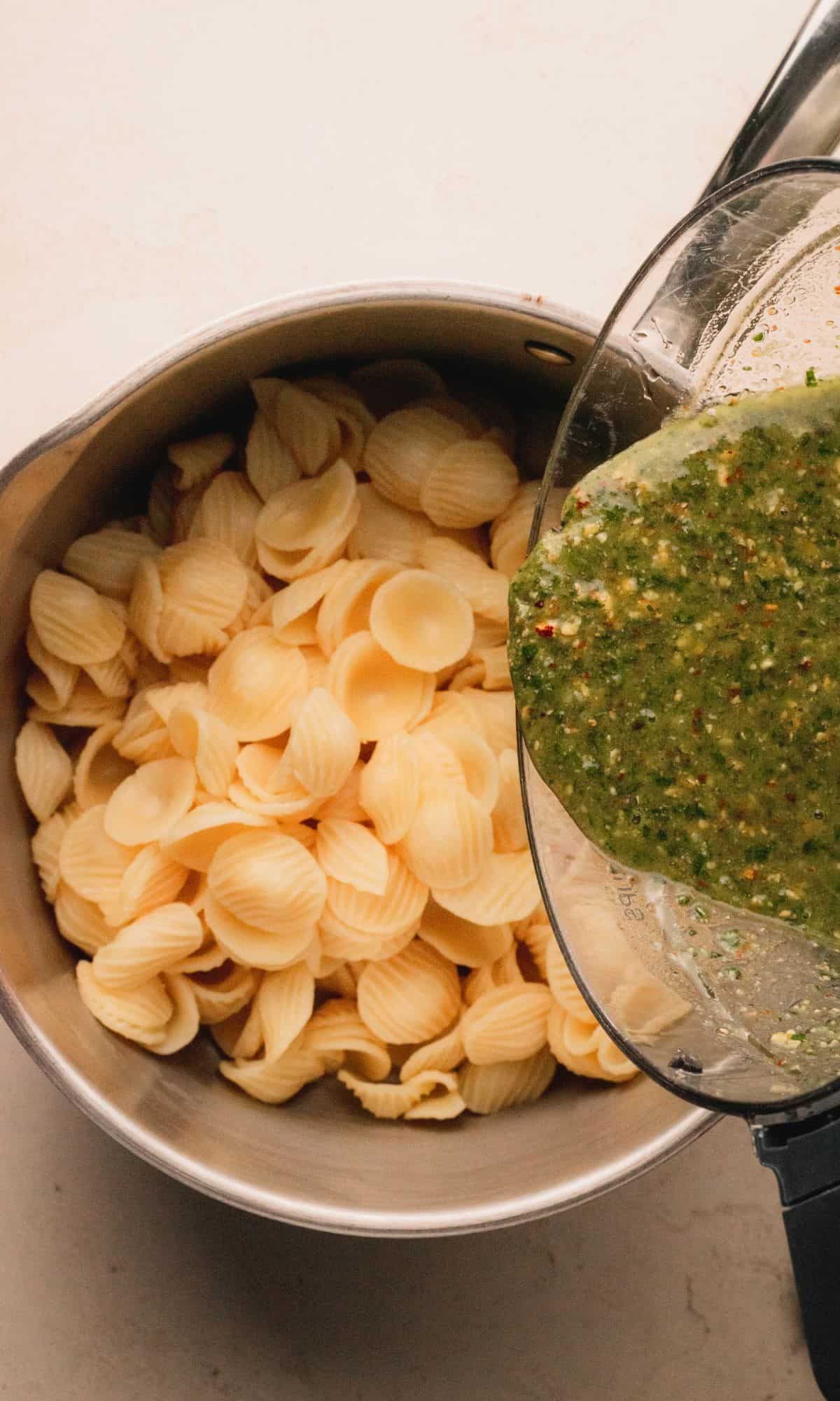 Adding parsley pesto to cooked pasta in a saucepan.