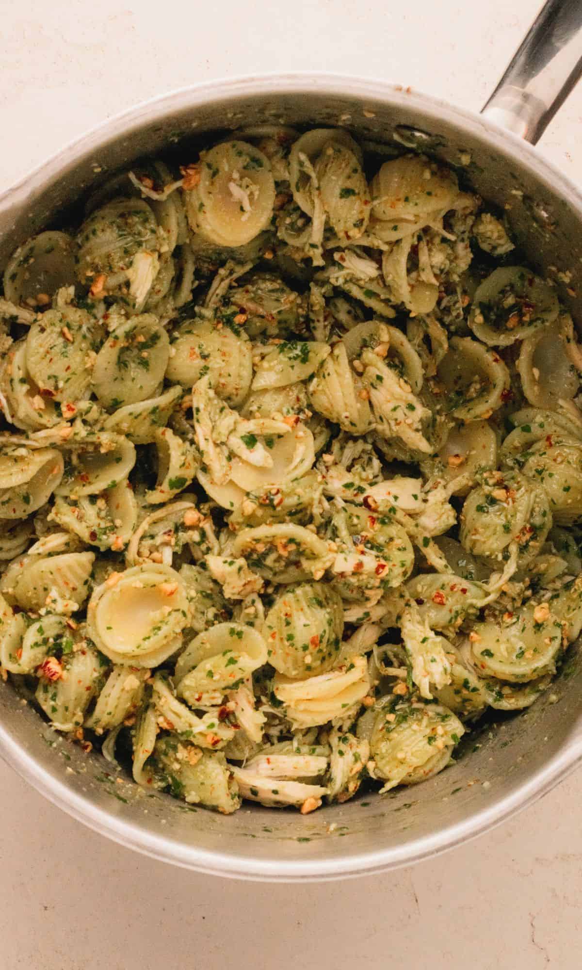 Parlsey pesto with chicken mixed with pasta in a saucepan.