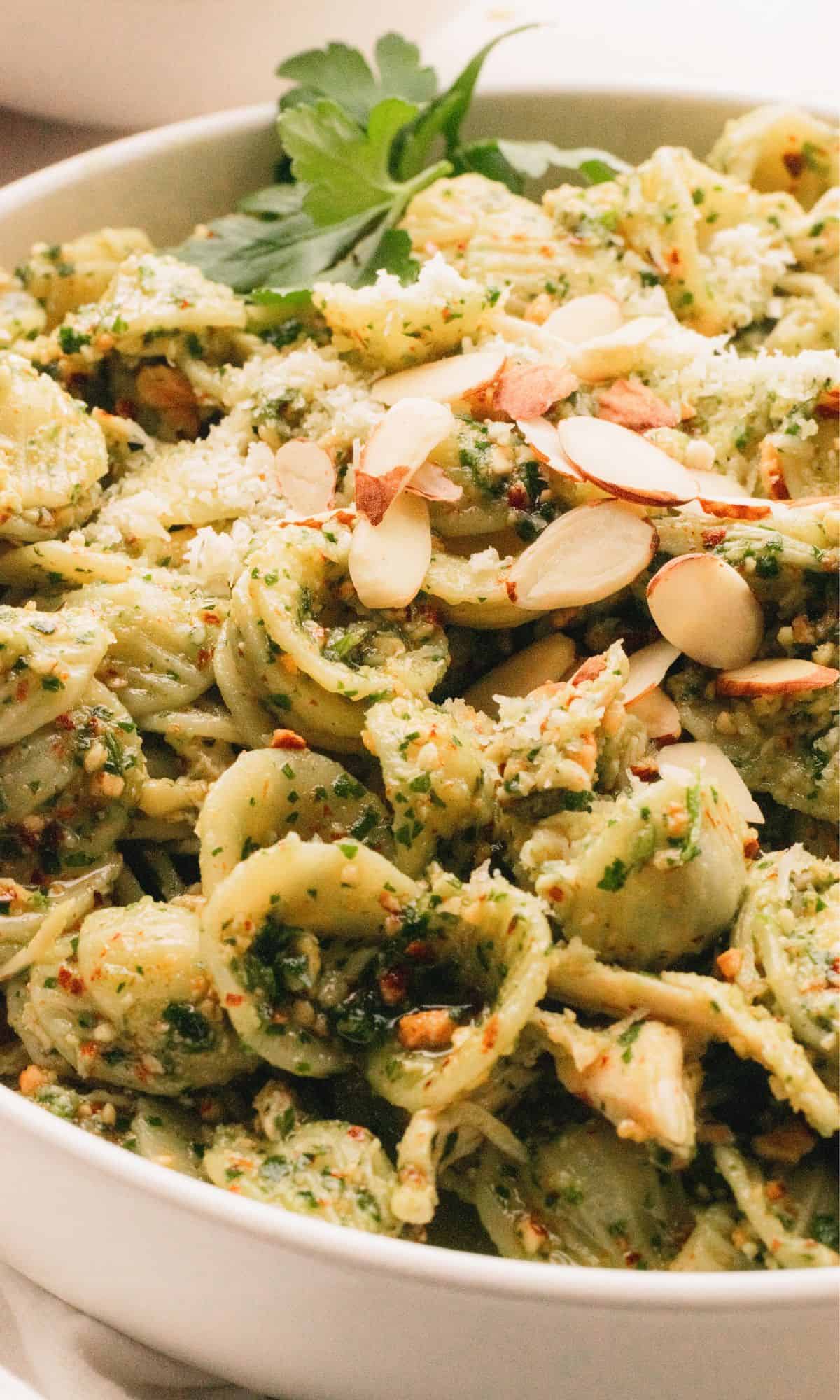 Parlsey pesto pasta in white bowl topped with almonds.