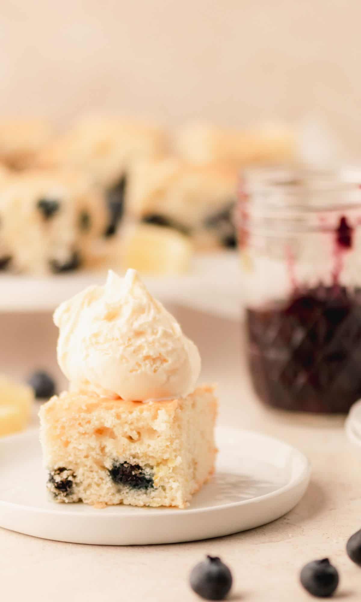 A piece of buttermilk cake with blueberries and a scoop of ice cream on top on a white plate.
