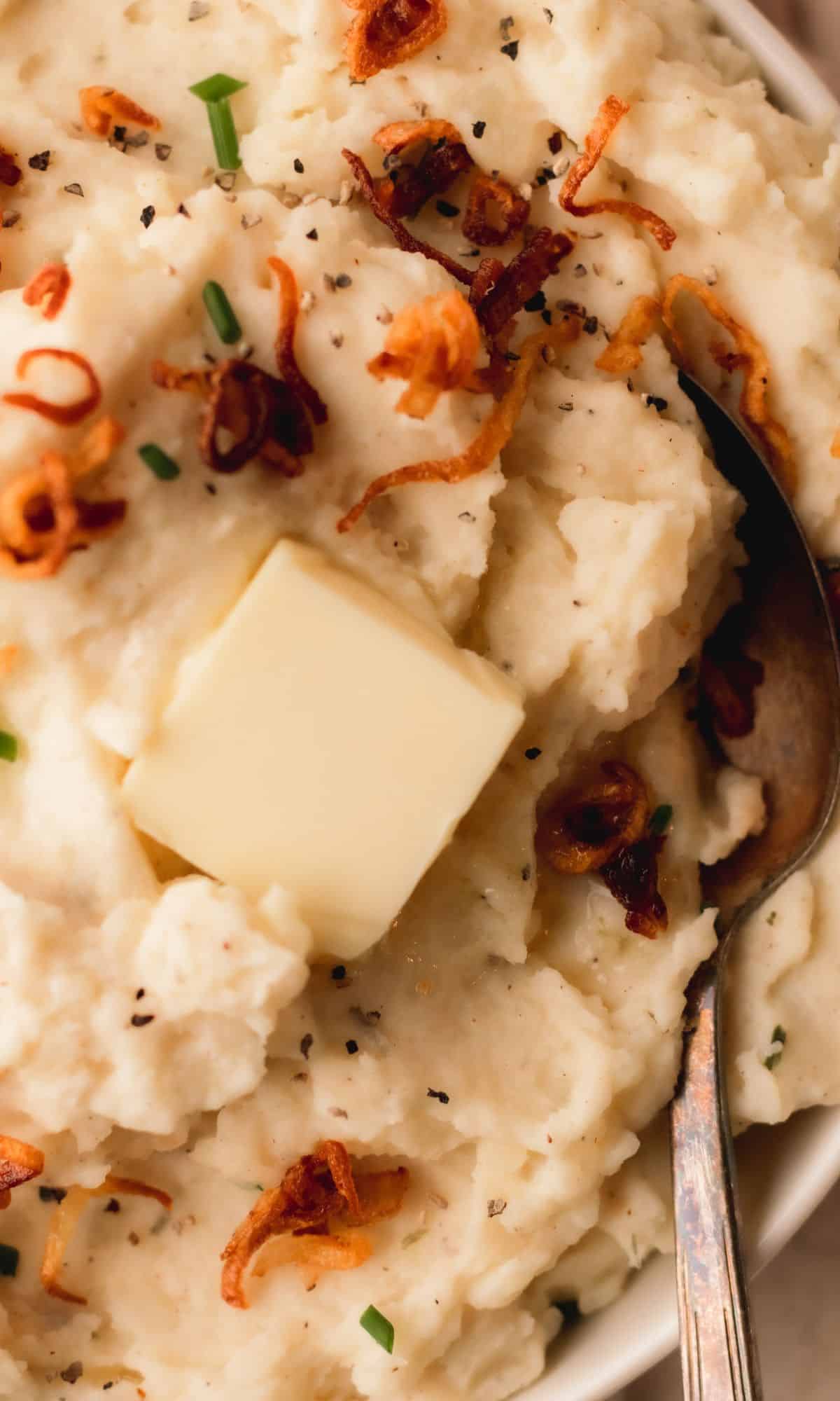 A bowl of mashed potatoes topped with crispy shallots and chives.