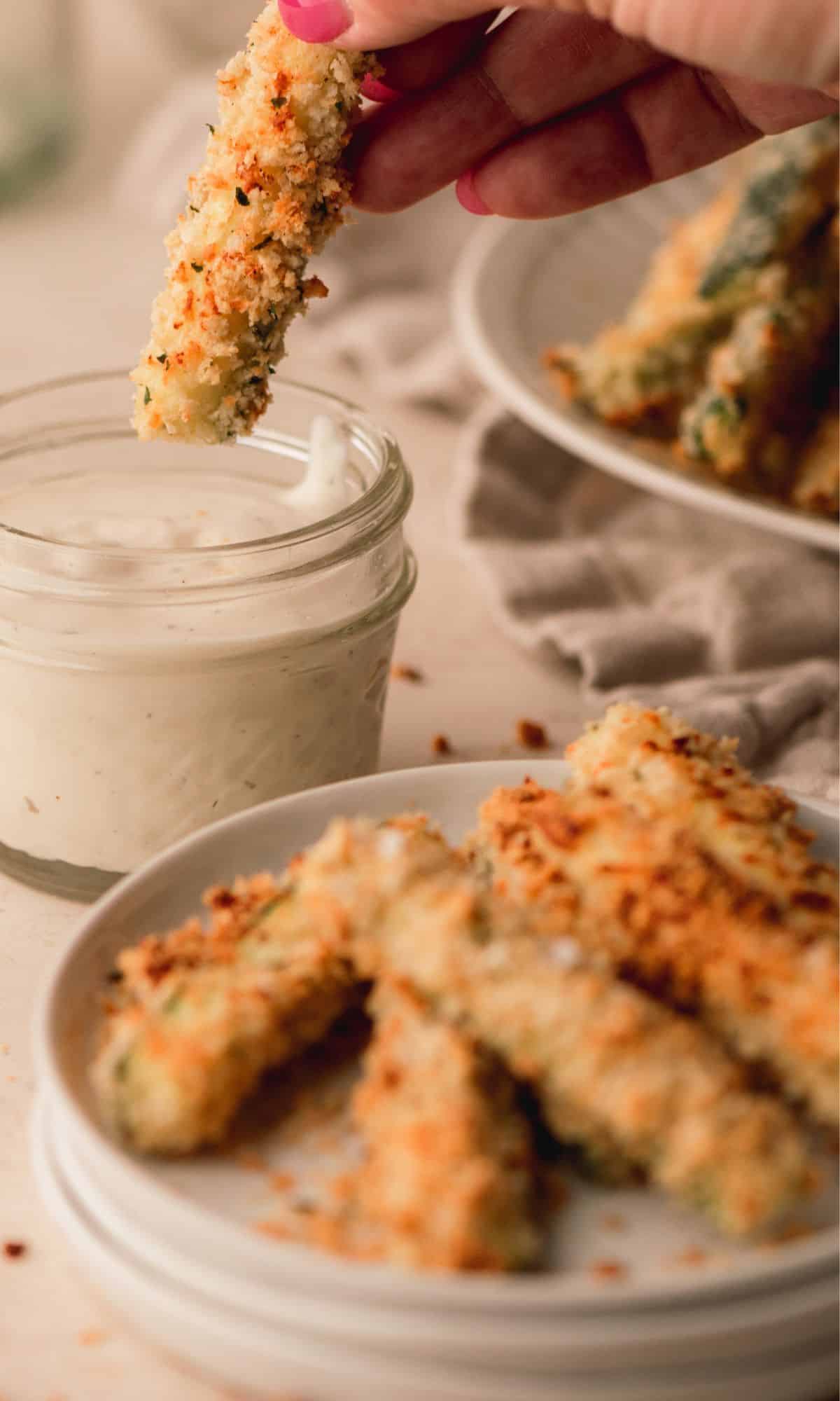 Zucchini fry getting dipped in ranch dressing.
