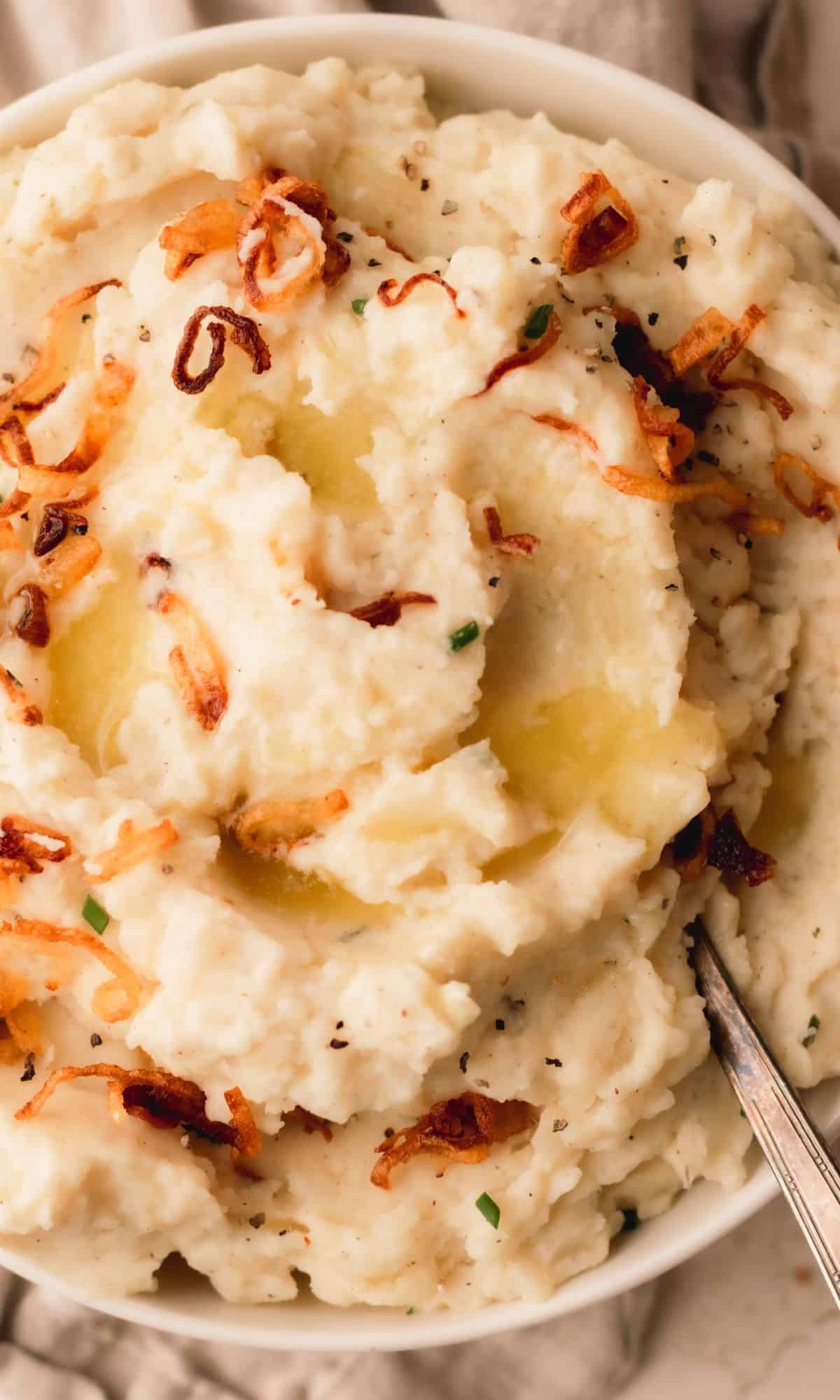 A bowl of mashed potatoes topped with crispy shallots and chives.