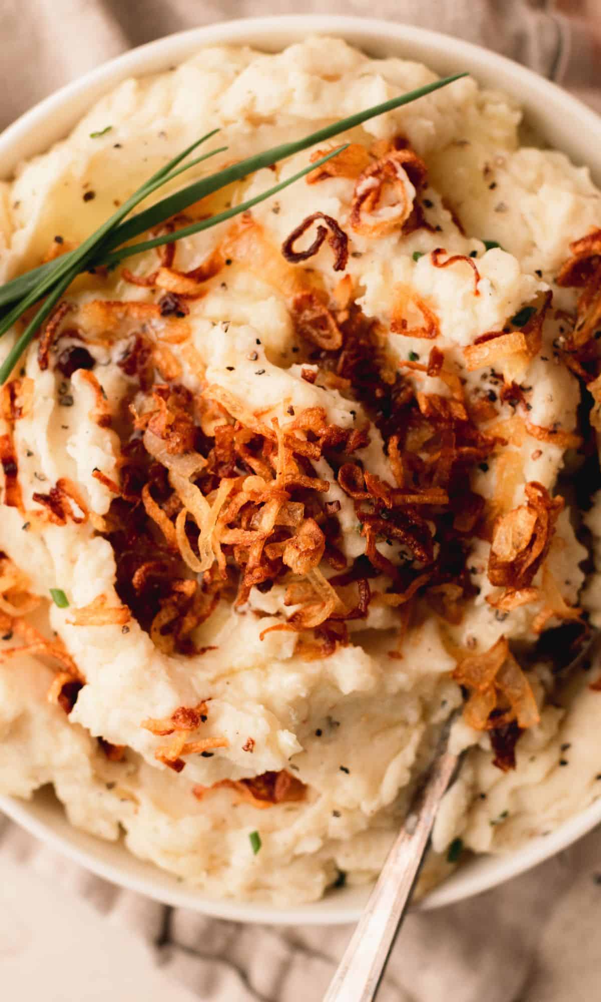 A bowl of mashed potatoes topped with crispy shallots and chives.