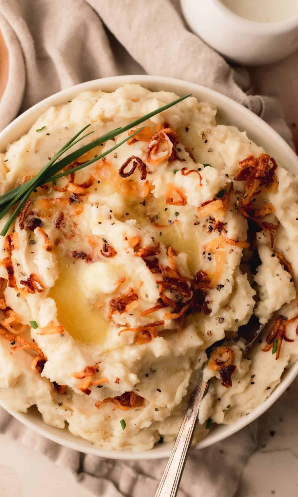 A bowl of mashed potatoes topped with crispy shallots and chives.