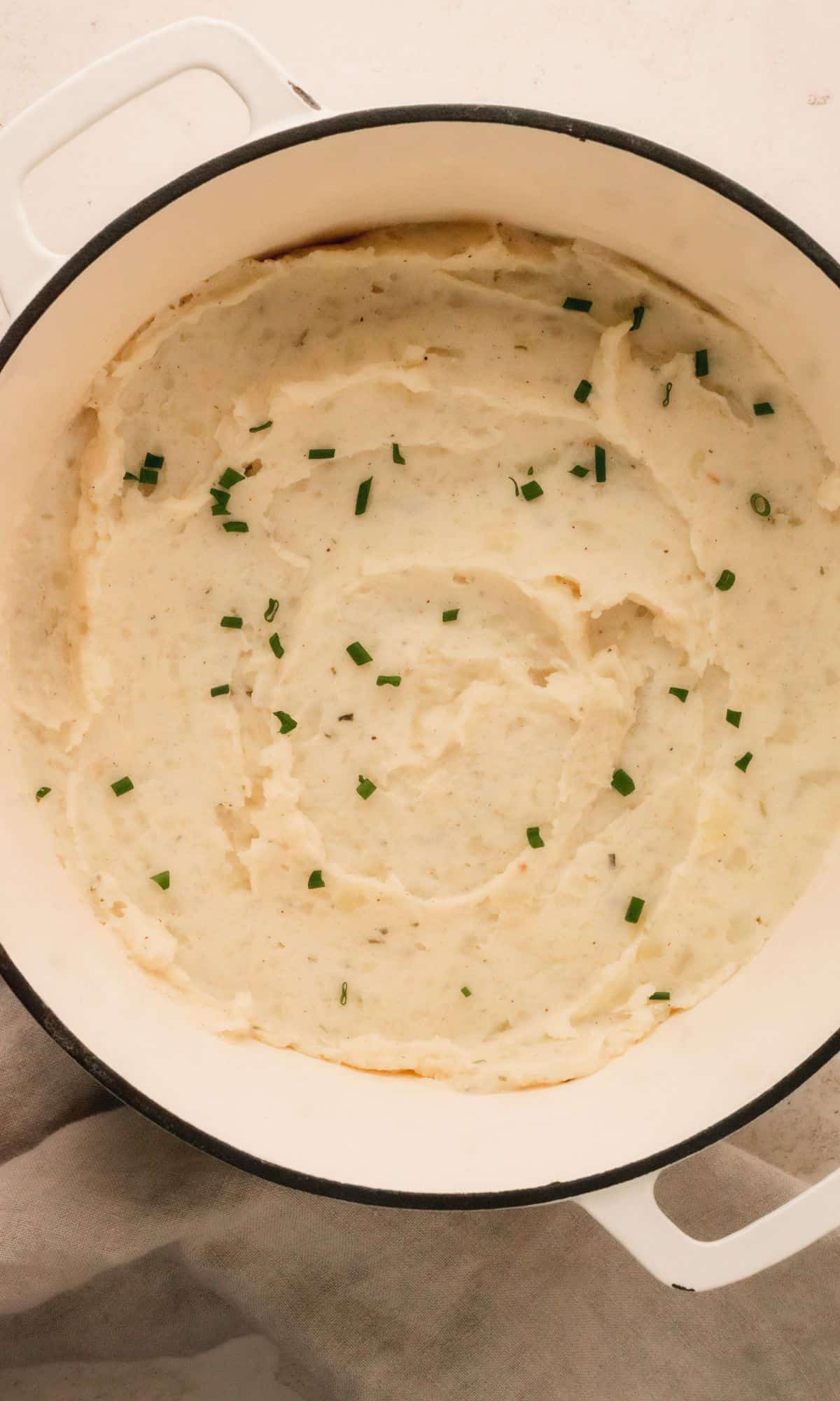 Mashed potatoes in a white dutch oven topped with chives.