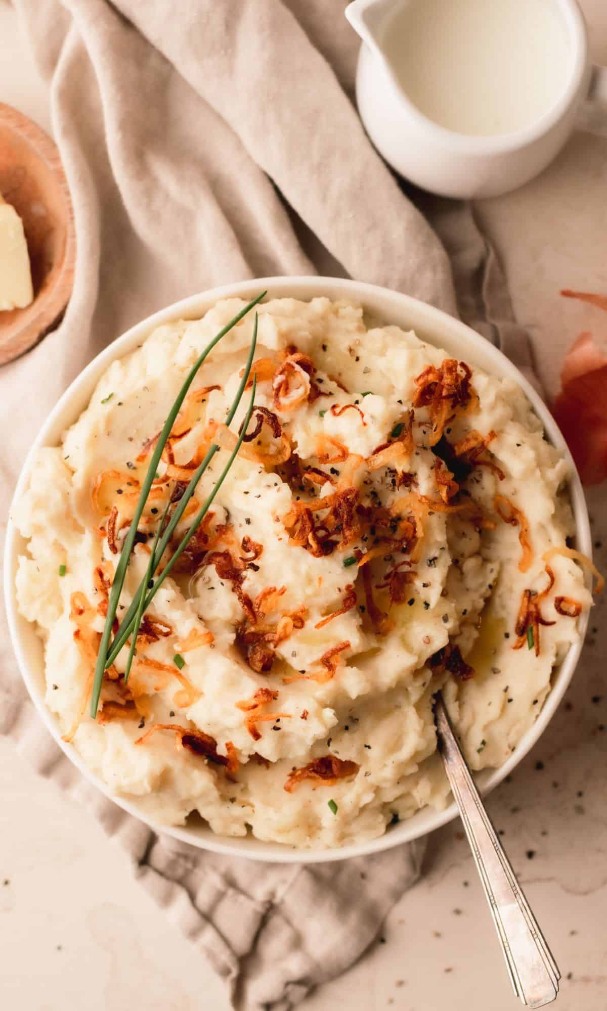 A bowl of mashed potatoes topped with crispy shallots and chives.