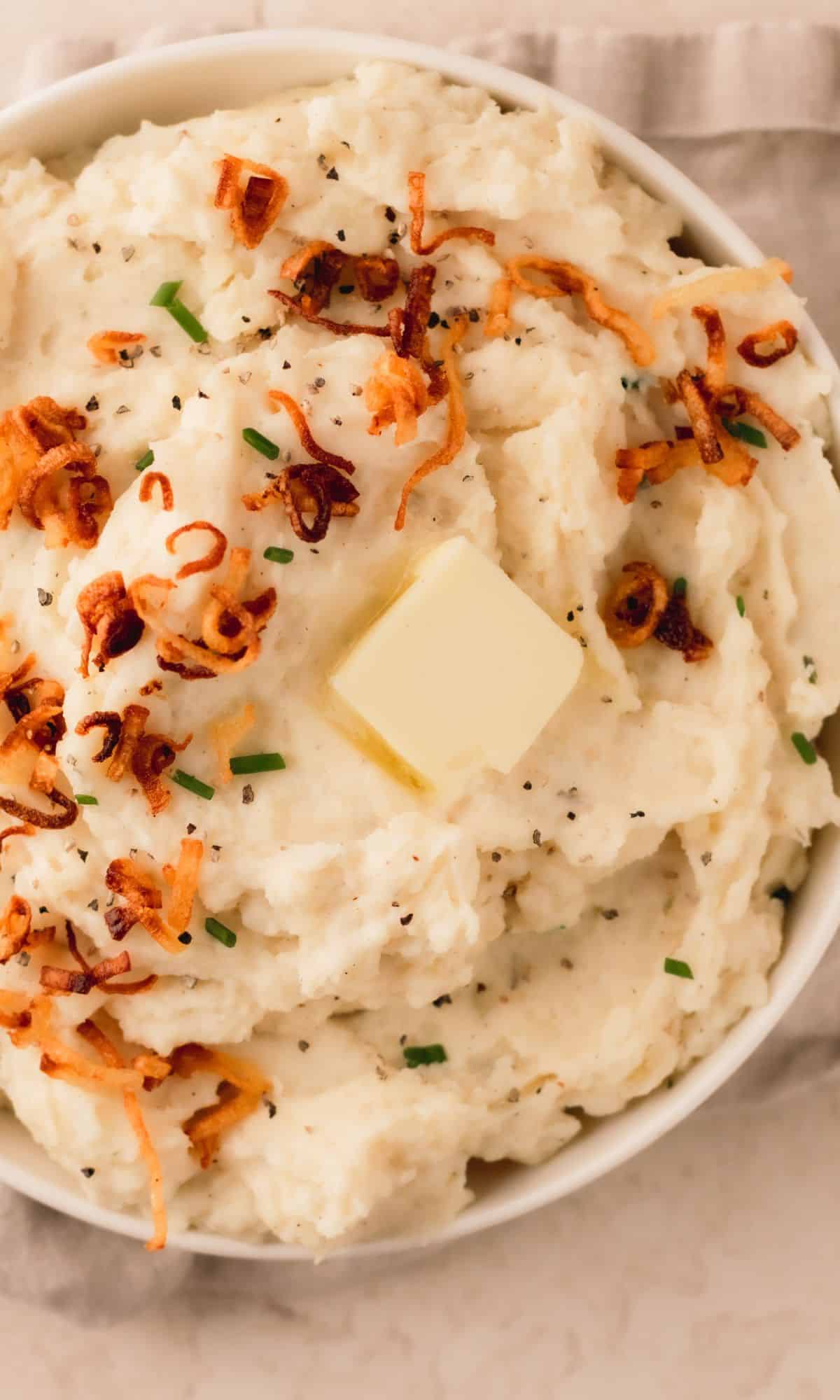 A bowl of mashed potatoes topped with crispy shallots and chives.