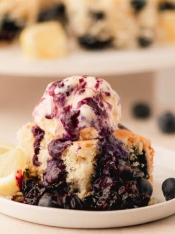 Buttermilk cake with blueberries and a scoop of ice cream and blueberry compote drizzled on top.