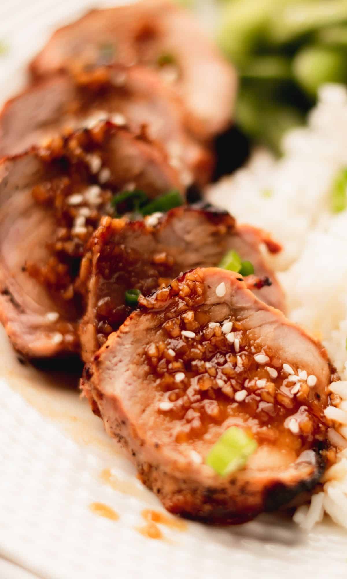 Honey garlic pork tenderloin garnished with sesame seeds on a white plate.