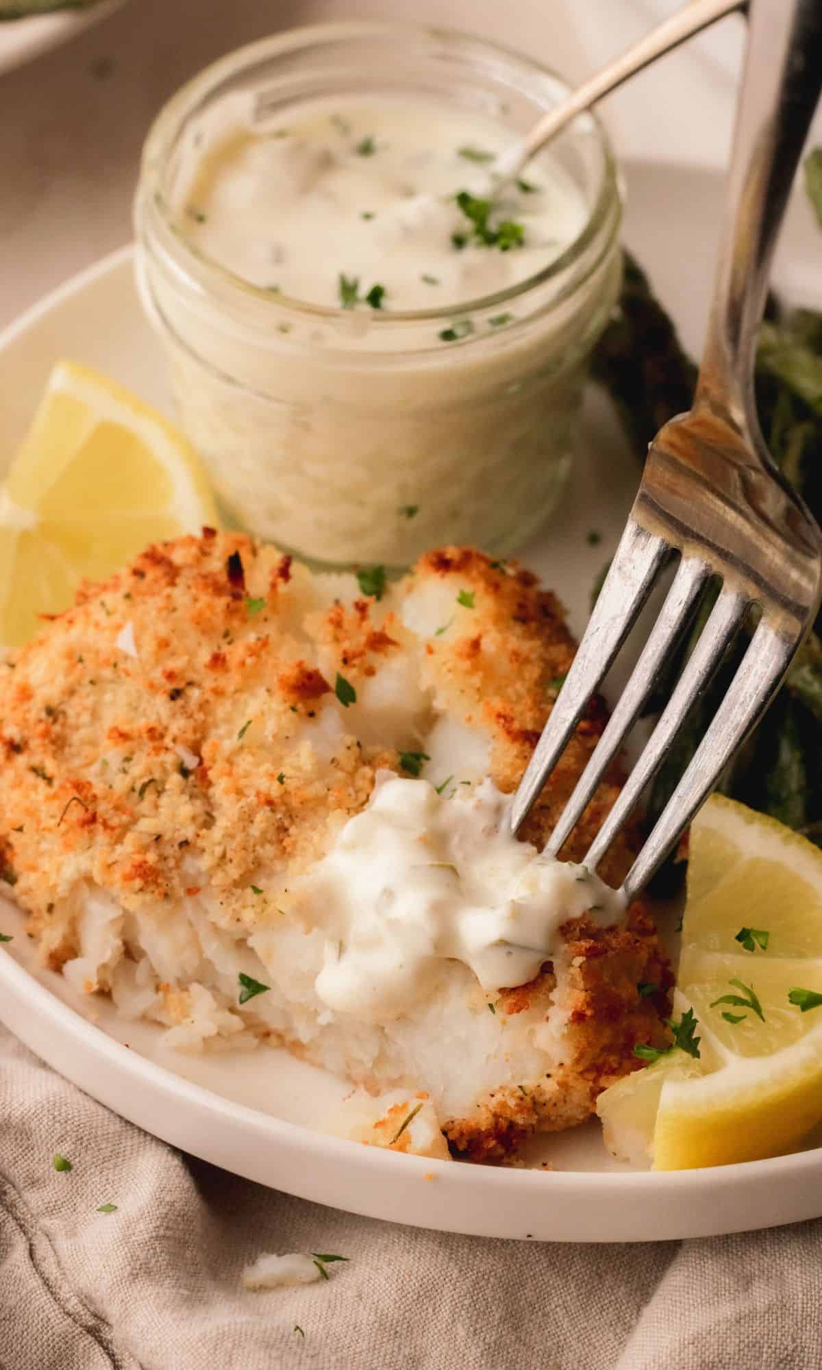 Parmesan baked cod on a white plate with a jar of tartar and green beans.