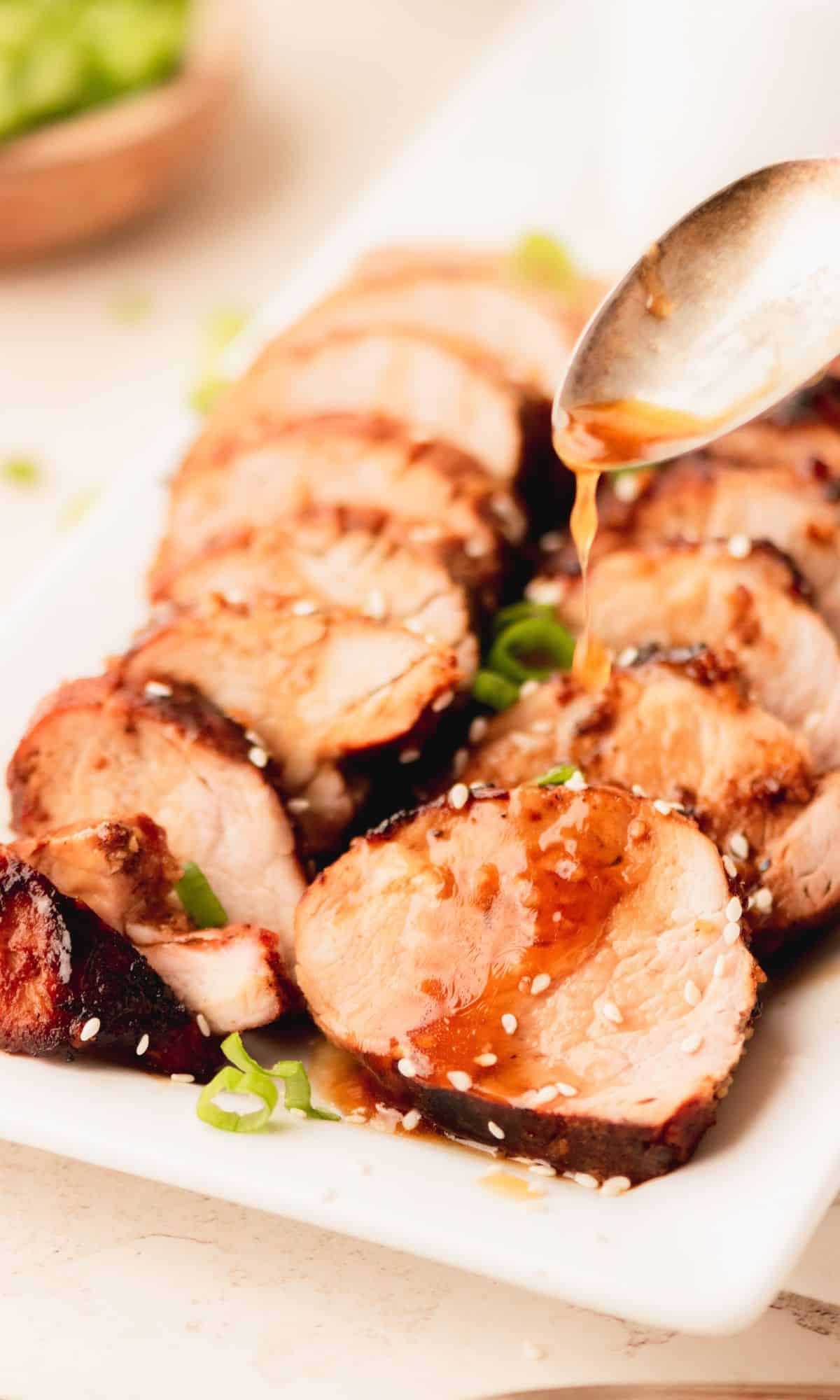 Honey garlic pork tenderloin garnished with sesame seeds on a white plate.