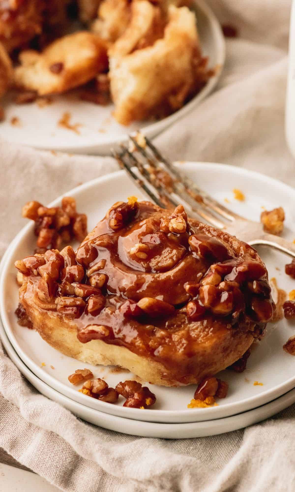 A caramel pecan sticky bun on a white plate with a fork.