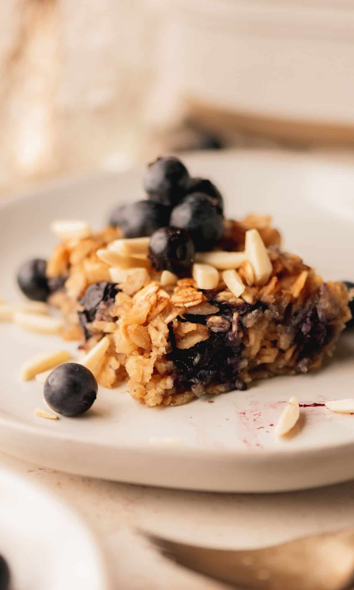 A slice of baked oatmeal on a white plate topped with blueberries and almonds.