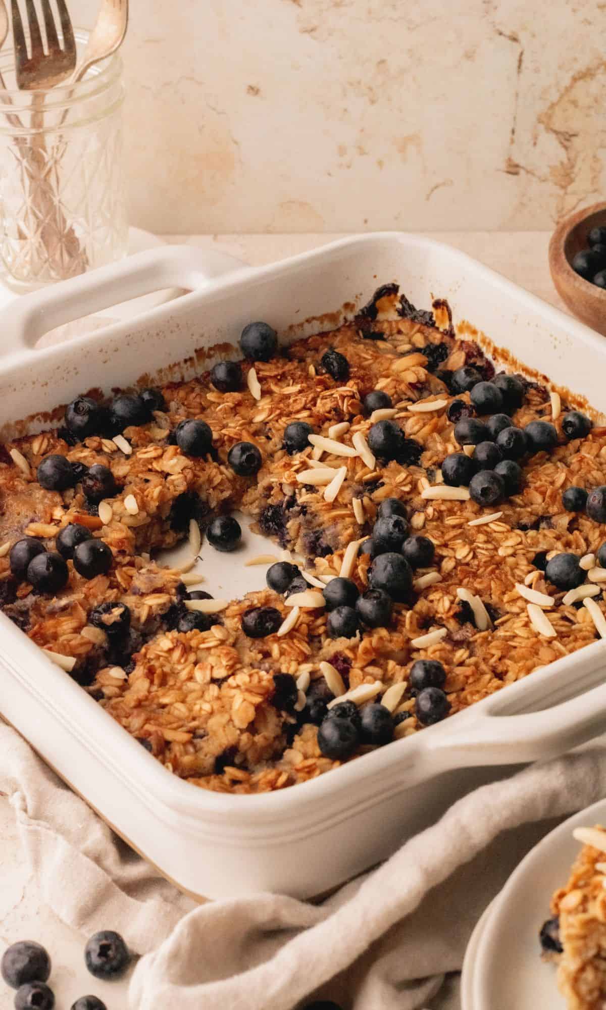 Banana blueberry baked oats in white baking dish with a slice removed.