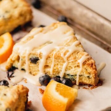 A blueberry scone surrounded by blueberries and pieces of orange.
