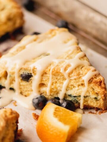 A blueberry scone surrounded by blueberries and pieces of orange.