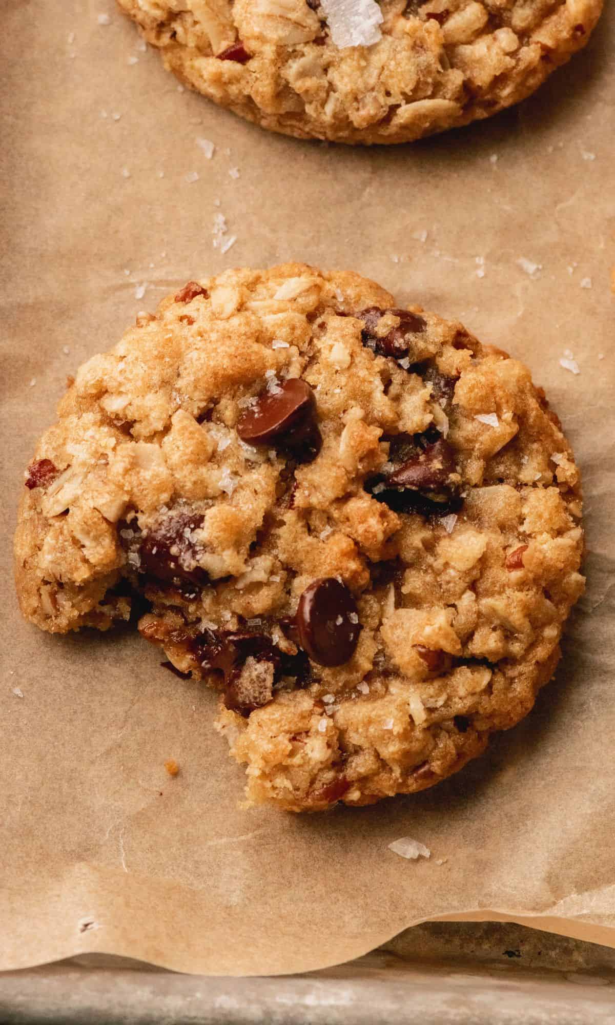 An oatmeal chocoalte chip cookie with a bite take out of it on a baking sheet.