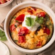 An individual egg bake in a white ramekin topped with sour cream and cilantro.