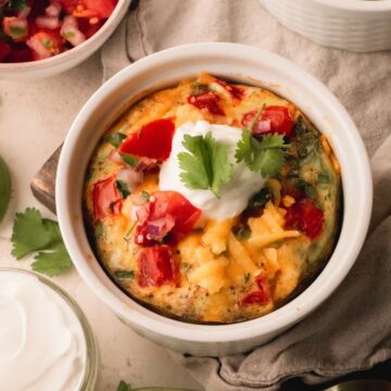 An individual egg bake in a white ramekin topped with sour cream and cilantro.