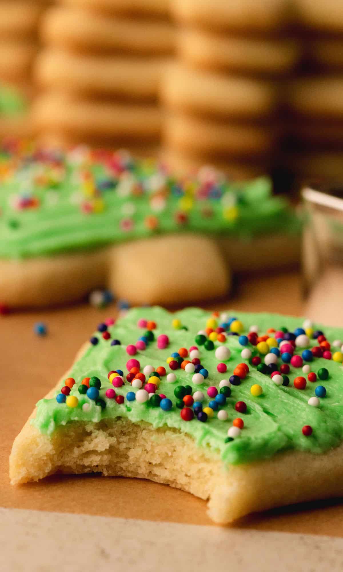 A frosted cookie with sprinkles with a bite taken out of it.