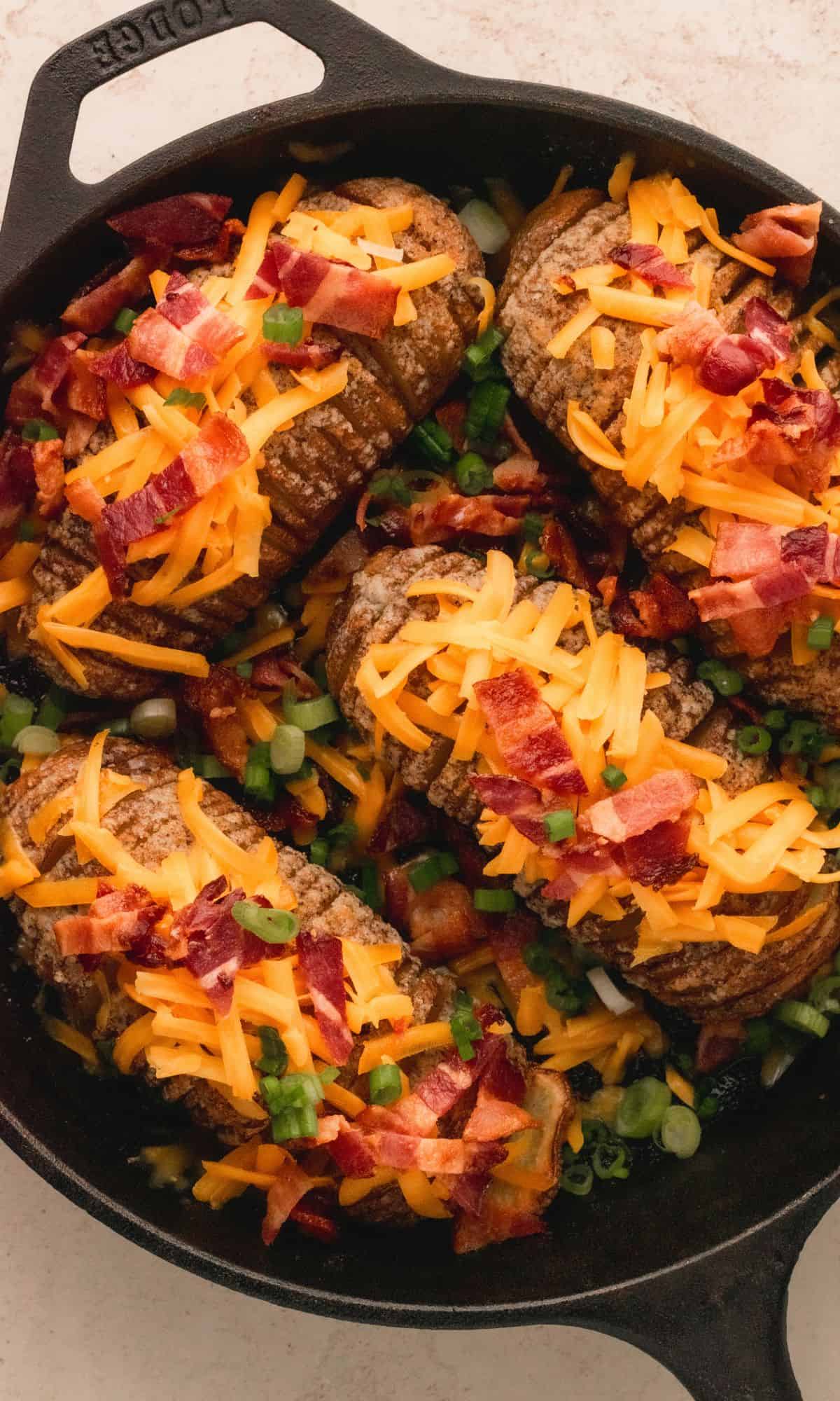 Hasselback potato with cheese and bacon in cast iron skillet.