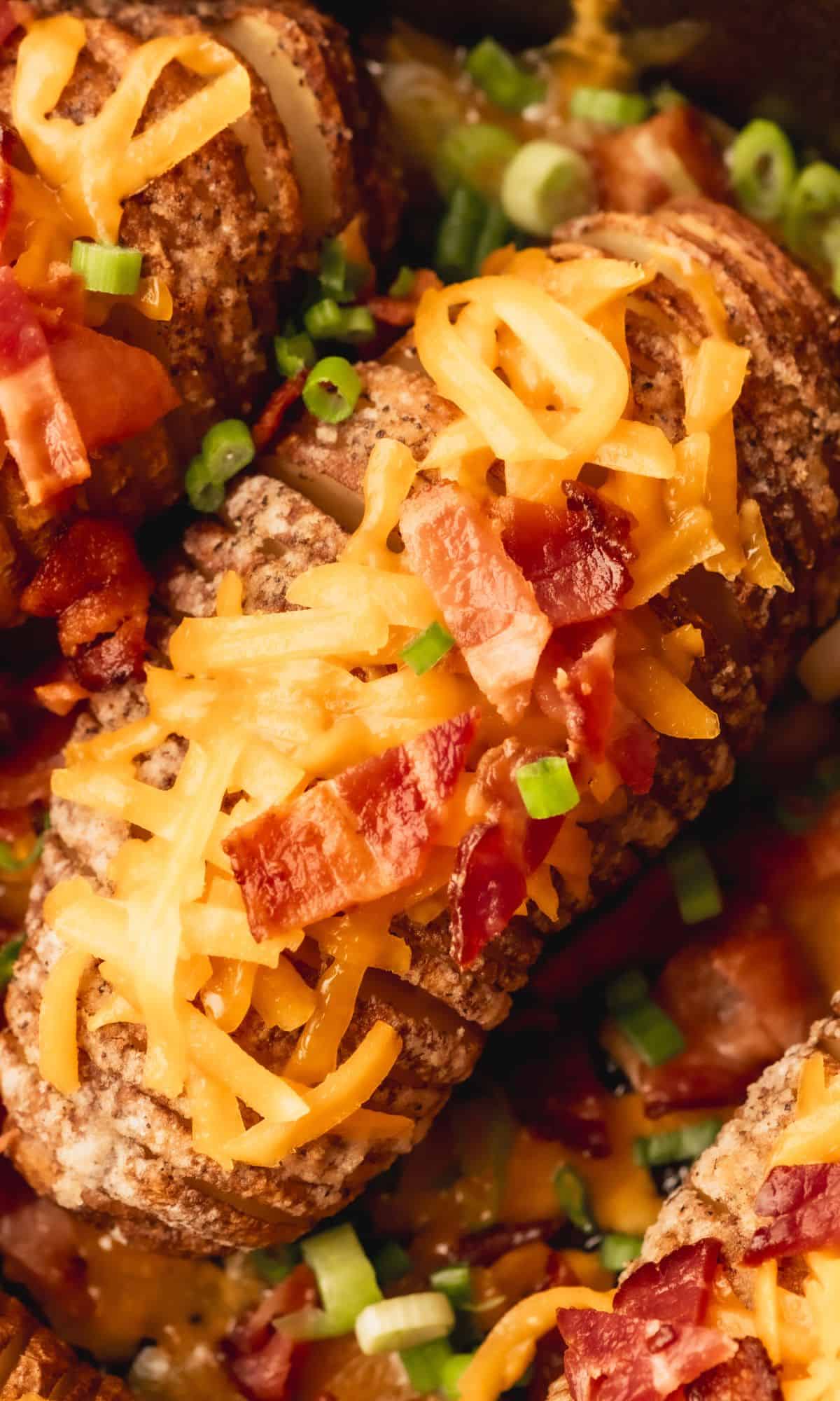 Hasselback potato with cheese and bacon in cast iron skillet.