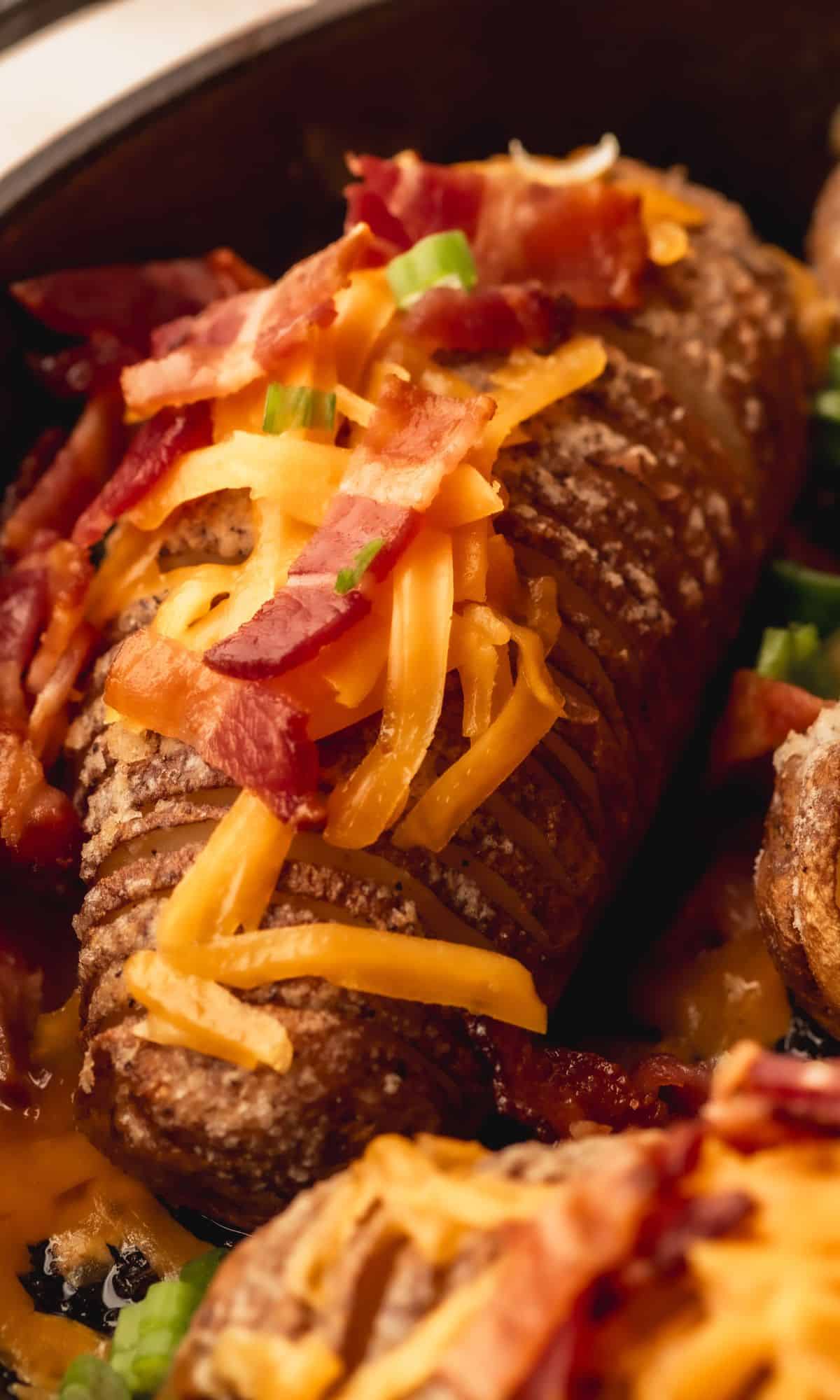 Hasselback potato with cheese and bacon in cast iron skillet.