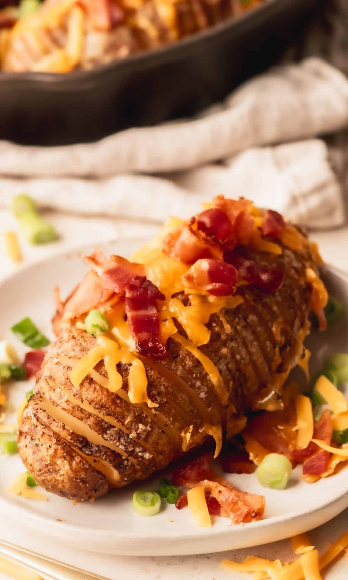 Hasselback potato with cheese and bacon on a white plate.