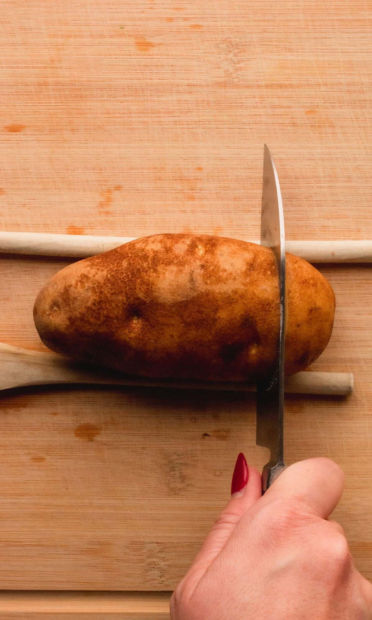 Slicing potato with wooden spoons on each side as a guide.