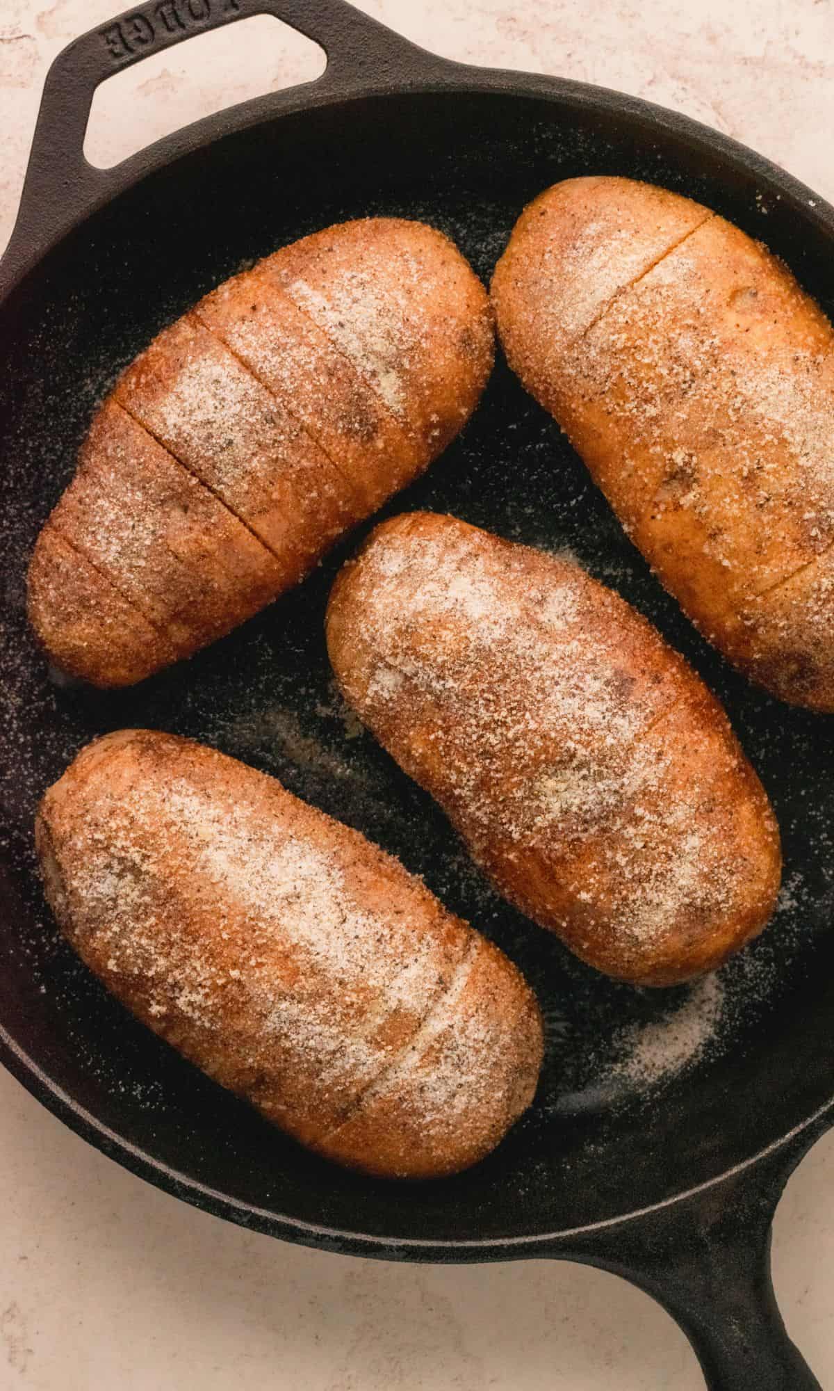 Hasselback potato with cheese and bacon in cast iron skillet.