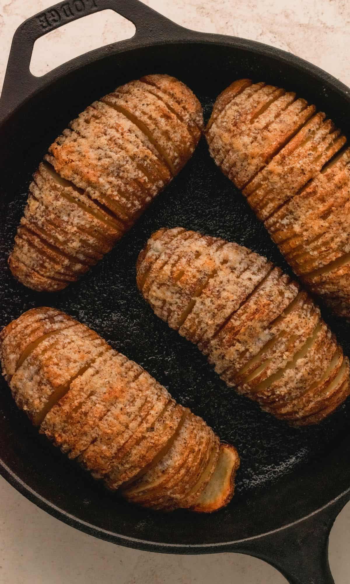 Hasselback potato with cheese and bacon in cast iron skillet.