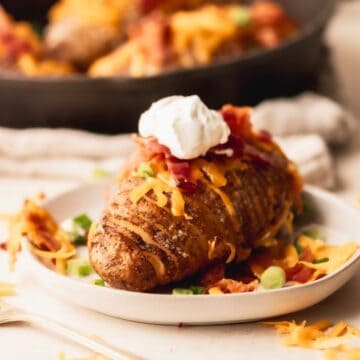 Hasselback potato with cheese, bacon and sour cream on a white plate.