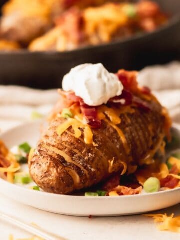 Hasselback potato with cheese, bacon and sour cream on a white plate.