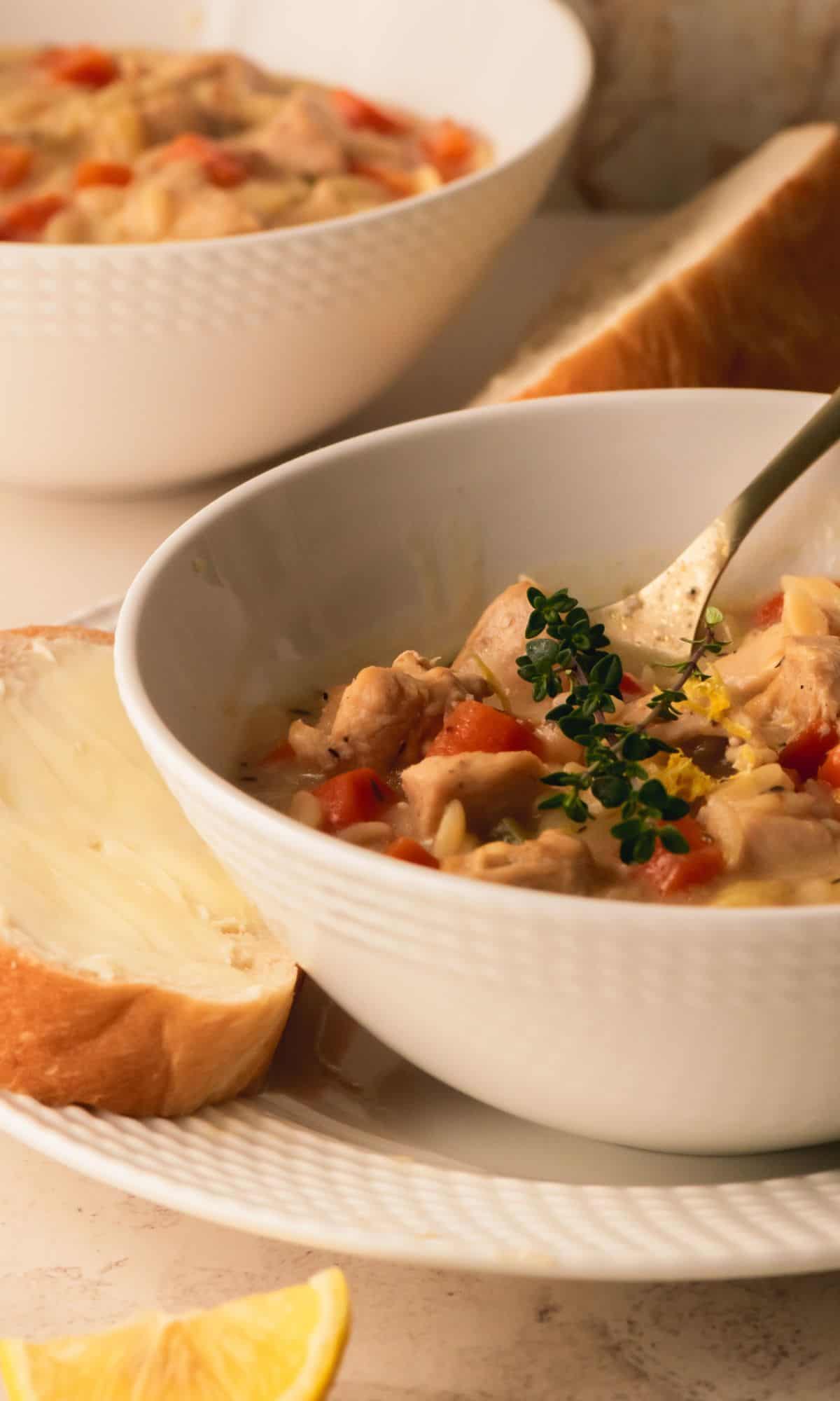 Chicken orzo soup in a white bowl with buttered bread on the side.