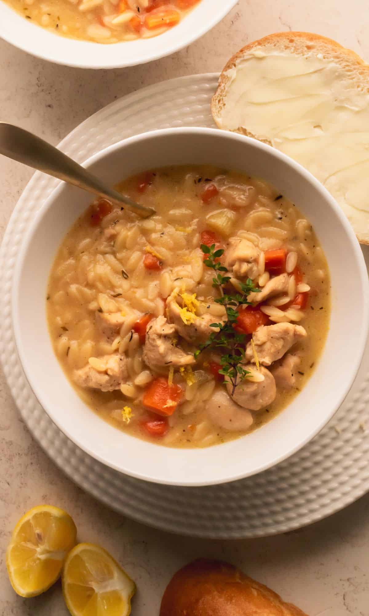 Chicken orzo soup in a white bowl with buttered bread on the side.