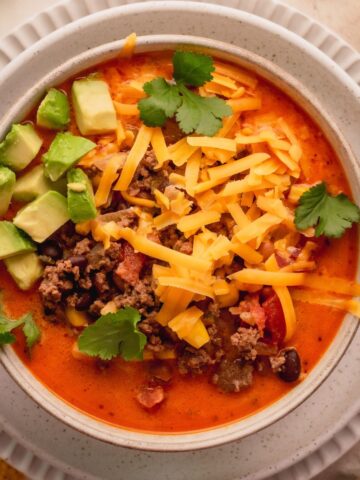 Taco soup in a white bowl topped with avocado, cheese and cilantro.
