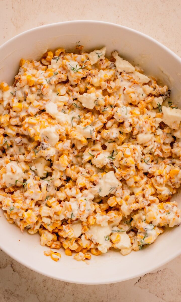 Corn and dressing mixed together in white bowl.