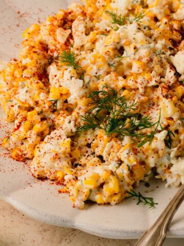 Corn salad on a white plate topped with fresh dill.
