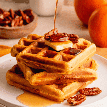 A stack of three waffles topped with butter, pecans and a drizzle of maple syrup.