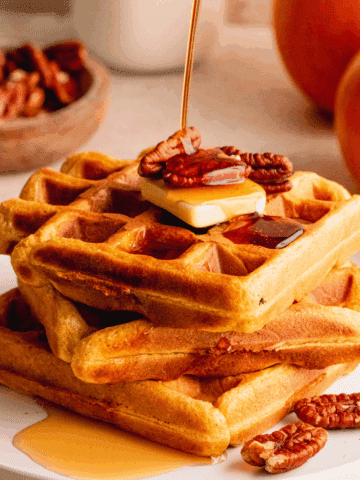 A stack of three waffles topped with butter, pecans and a drizzle of maple syrup.