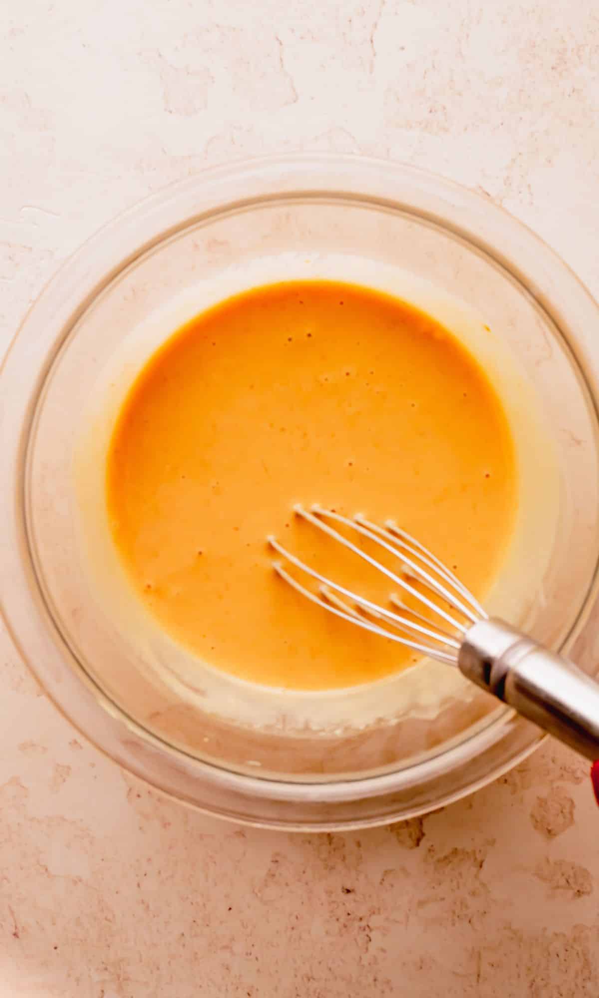 Honey mustard sauce mixed in a bowl with a whisk.