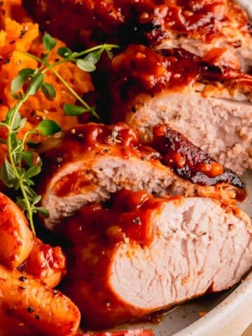 Sliced pork tenderloin on a plate with sweet potatoes and apples.