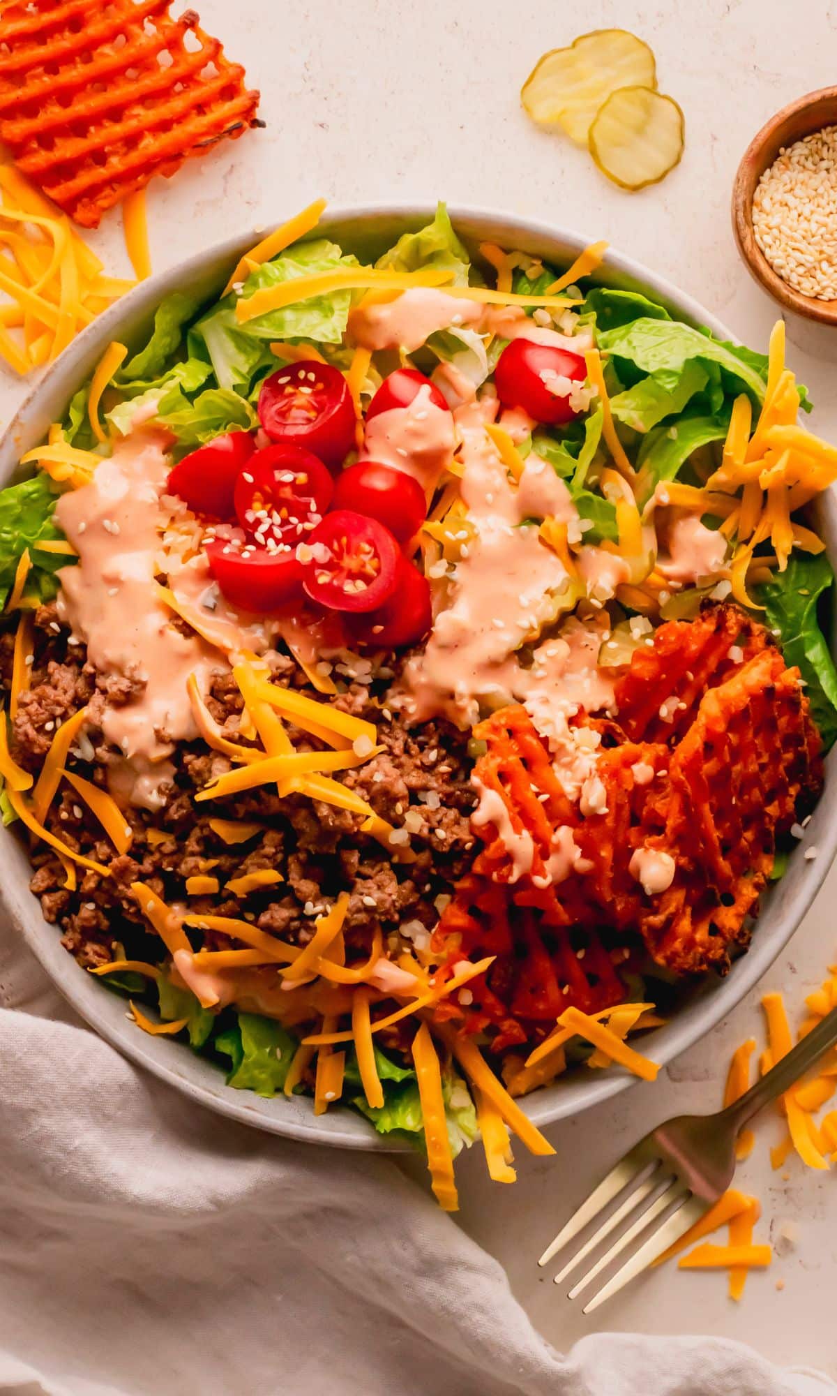 A cheeseburger salad topped with cheese and sweet potato fries.